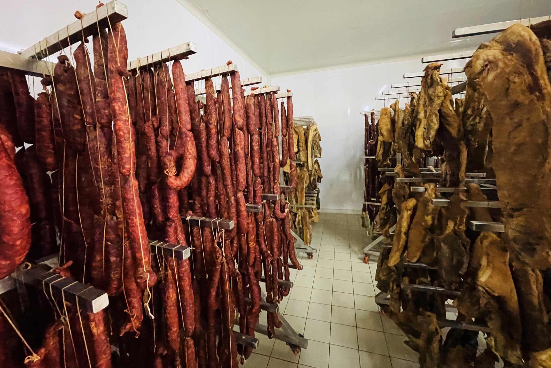 Many rows of sausages hanging from wooden bars aging within a sausage room in Albania